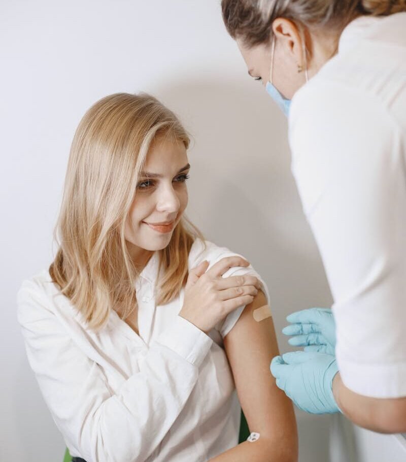 A young woman smiles as she receives a vaccination from a healthcare professional wearing gloves.